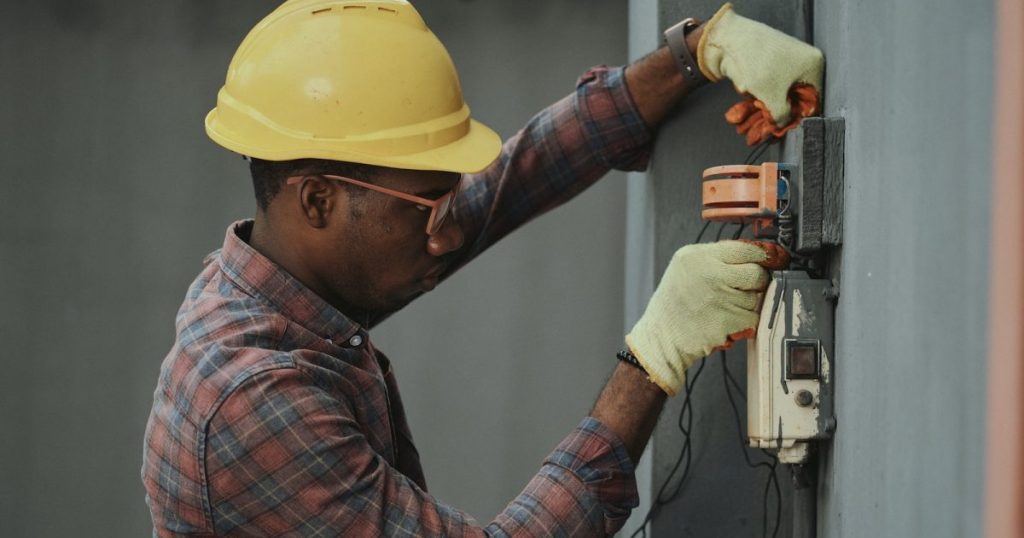 What Does M&E Stand For in Construction? : man in brown and white plaid dress shirt and yellow hard hat holding black and orange