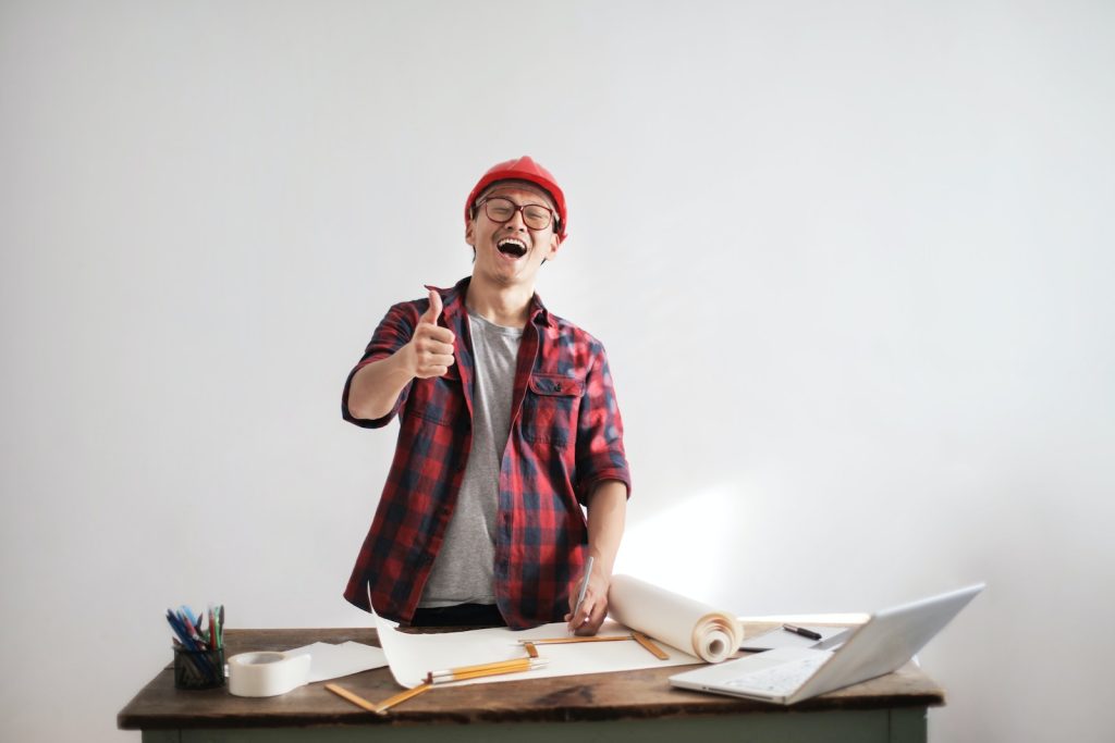Laughing male constructor showing thumb up at working desk, Construction Bonds
